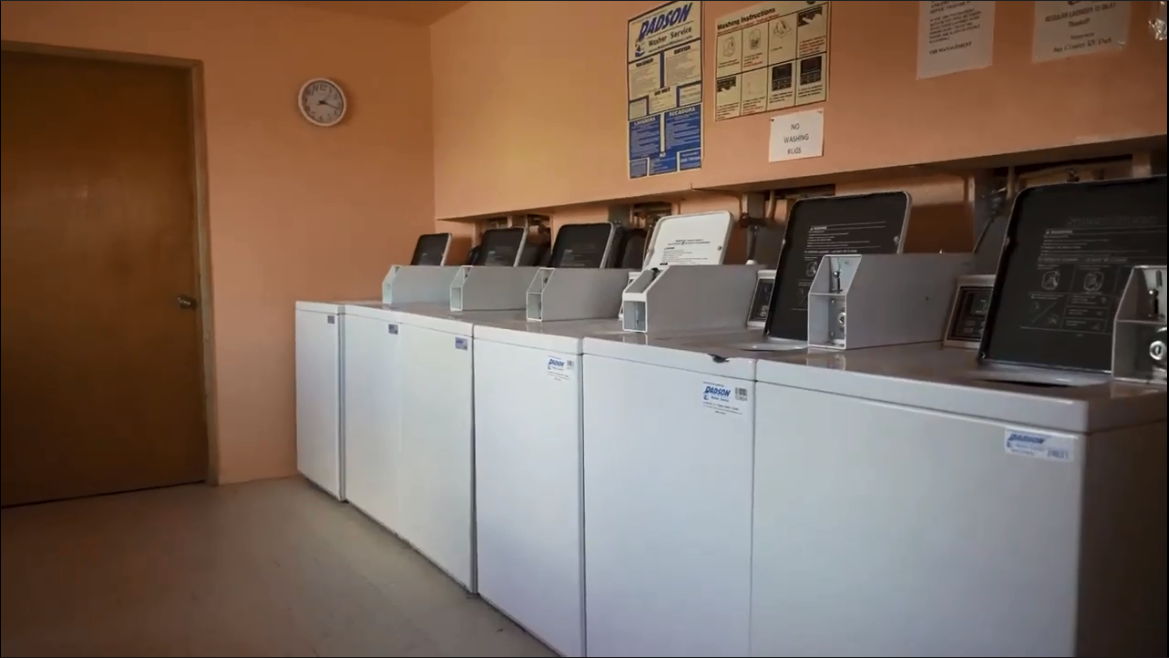 Six coin operated washing machines on one side of a laundry room.